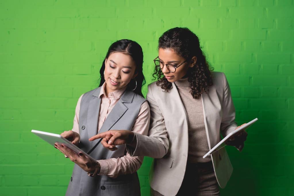 Африканские американские и азиатские бизнесвумен, работающие с цифровыми планшетами перед зеленой стеной
 - Фото, изображение