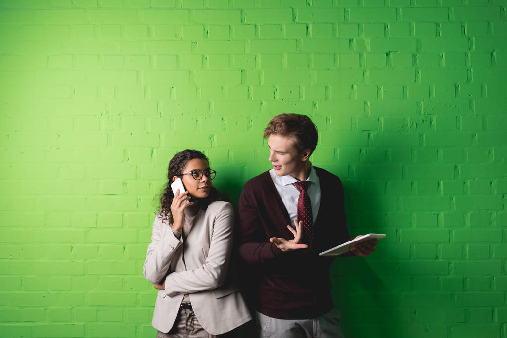 monietniset liikemiehet käyttävät digitaalista tablettia ja älypuhelinta vihreän seinän edessä
 - Valokuva, kuva