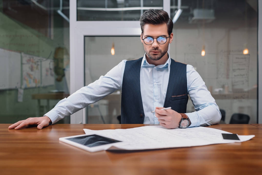 Erwachsener Geschäftsmann mit Brille arbeitet im Büro mit Blaupausen und Gadgets - Foto, Bild