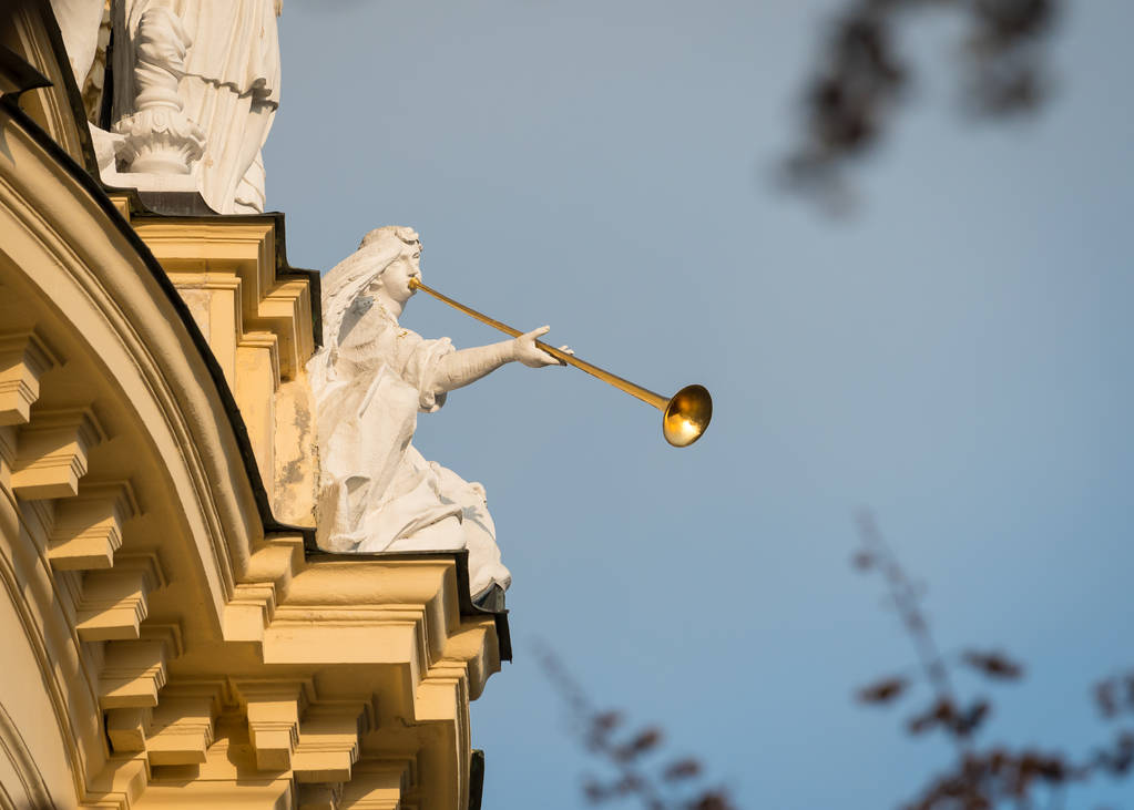 Каменная фигура с золотой трубой сидит на старом здании
 - Фото, изображение