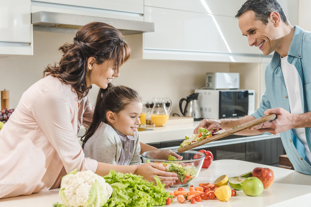 щаслива усміхнена сім'я робить салат разом на кухні
  - Фото, зображення