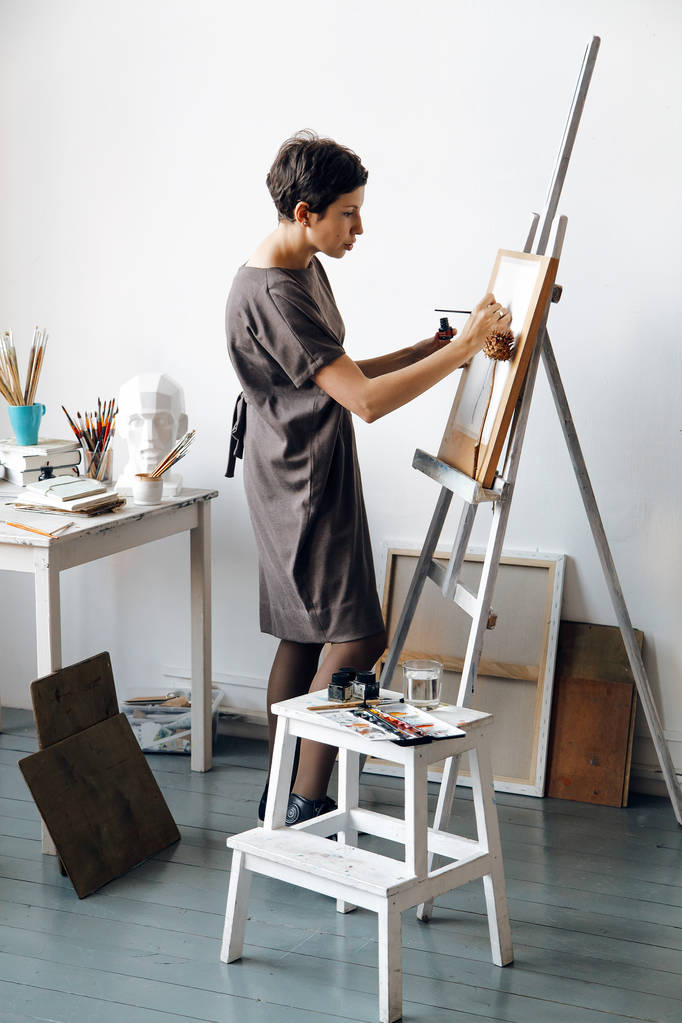 Artista femminile nel suo spazioso studio bianco che lavora con la pittura ad acquerello. Illuminazione naturale. Divulgazione del concetto di creatività. Composizione verticale
. - Foto, immagini