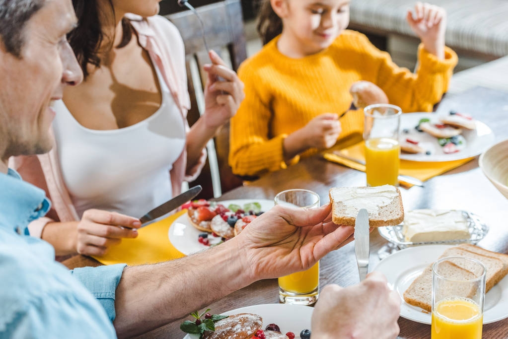 ευτυχισμένη οικογένεια κάθεται στο τραπέζι και τρώνε κρέπες με μούρα και χυμό - Φωτογραφία, εικόνα