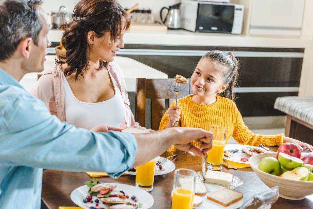 gelukkig gezin eten pannenkoeken aan tafel met SAP en fruit in de keuken - Foto, afbeelding