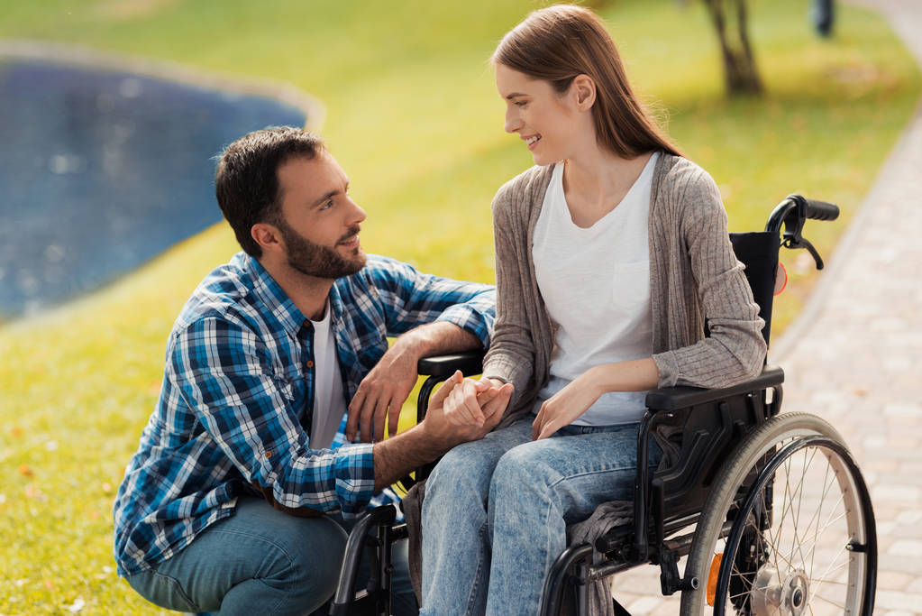 Bir kadın bir tekerlekli sandalyede oturuyor. Bir adam yanında oturan ve ellerini tutarak. - Fotoğraf, Görsel
