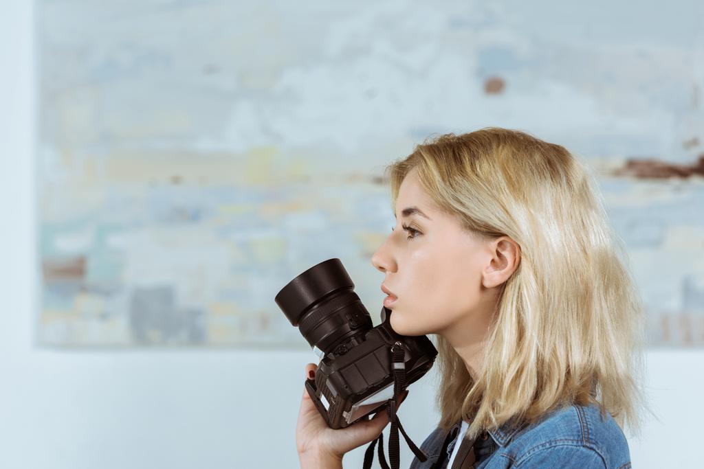 vista lateral de la mujer pensativa con cámara de fotos en la mano mirando hacia otro lado en el estudio
 - Foto, Imagen