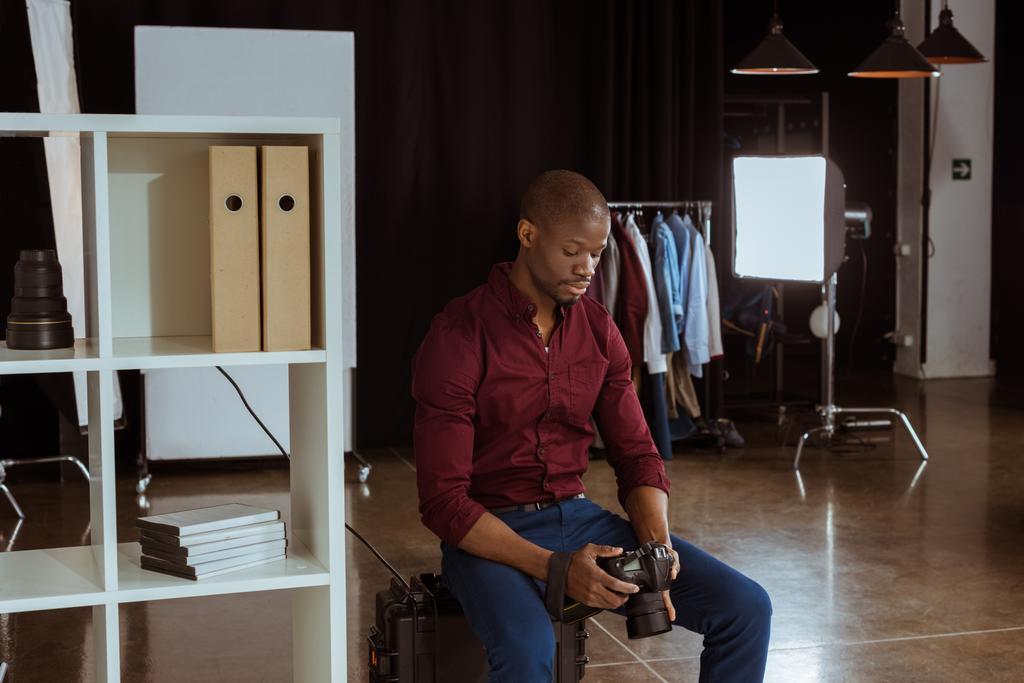 retrato de fotógrafo afroamericano mirando la cámara fotográfica en las manos mientras elige fotos en el estudio
 - Foto, imagen