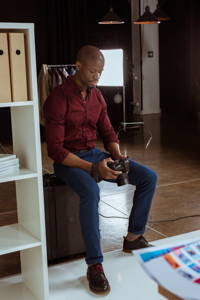 Αφρικανικός Αμερικανός φωτογράφος ψάχνει στο φωτογραφία κάμερα στα χέρια ενώ επιλέγοντας φωτογραφίες σε στούντιο - Φωτογραφία, εικόνα
