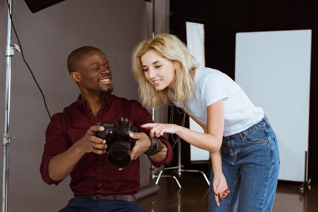 photographe afro-américain et modèle caucasien choisissant des photos ensemble pendant la séance photo en studio
 - Photo, image