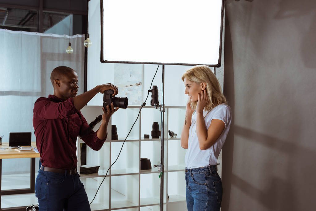 Αφρικανικός Αμερικανός φωτογράφος λήψη φωτογραφιών των ελκυστικό μοντέλο σε στούντιο - Φωτογραφία, εικόνα