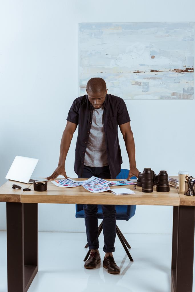 концентрований афроамериканський фотограф, дивлячись на фотосесію, стоячи на робочому місці
 - Фото, зображення