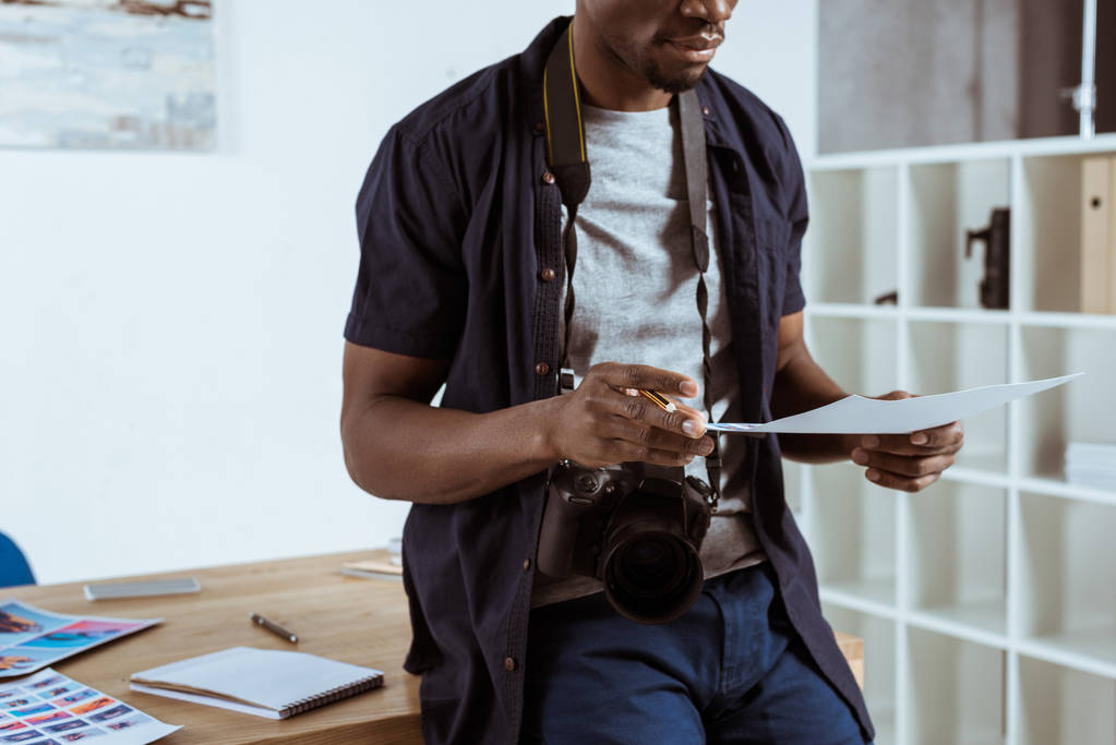 обрезанный снимок африканского американского фотографа с фотографиями в руках на рабочем месте
 - Фото, изображение