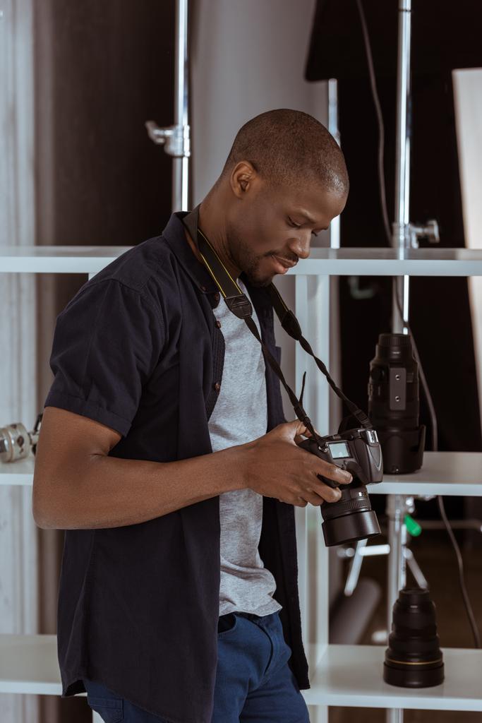 side view of african american photographer choosing photos on photo camera in studio - Photo, Image