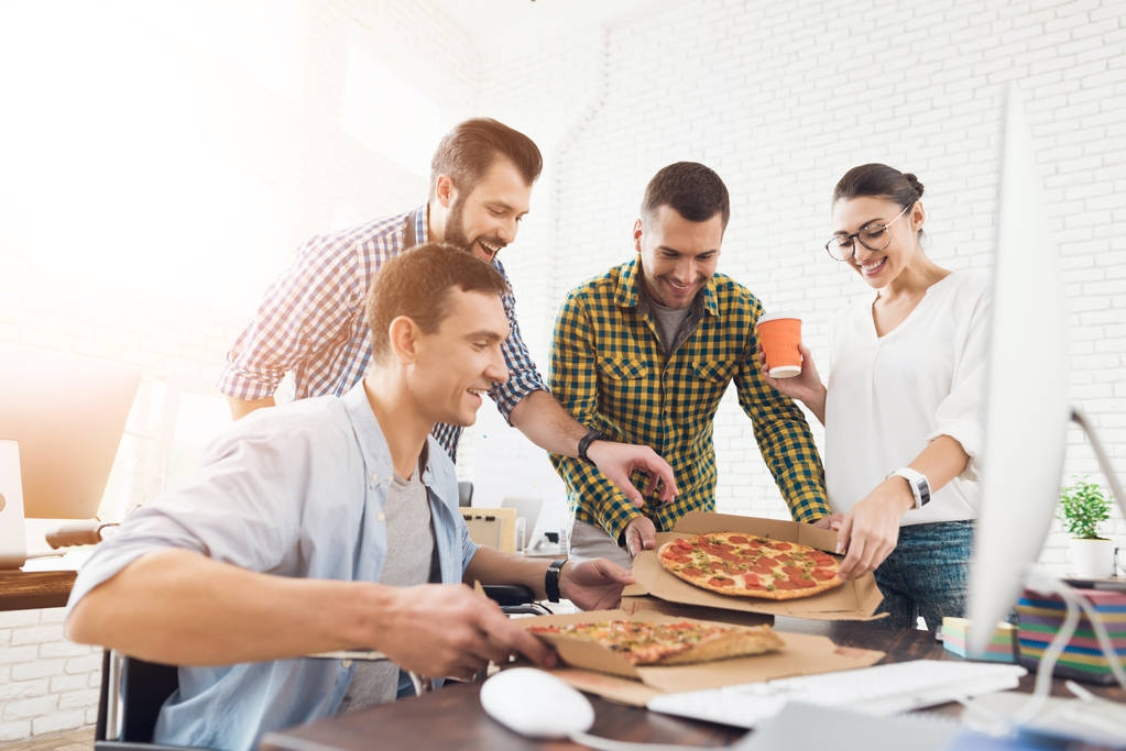 Irodai dolgozók és az ember egy tolószékben eszik pizzát. A világos és modern irodában dolgoznak. - Fotó, kép