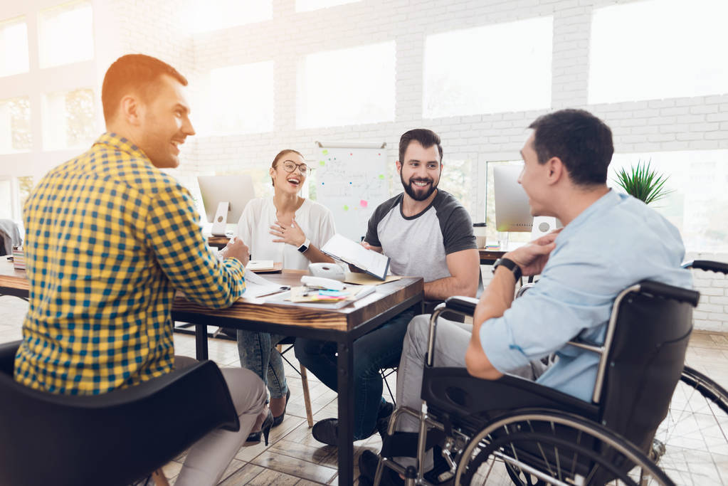 Un uomo in sedia a rotelle comunica allegramente con i dipendenti dell'ufficio durante una riunione di lavoro
. - Foto, immagini