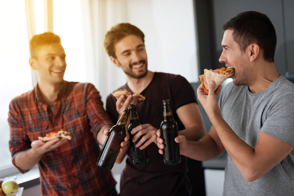 Gli uomini bevono birra e mangiano pizza in cucina. Parlano e si divertono
. - Foto, immagini