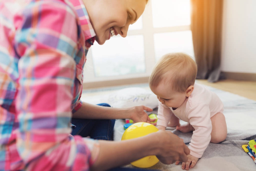 Una donna in camicia rosa si siede sul pavimento nel soggiorno e gioca con il suo bambino
. - Foto, immagini