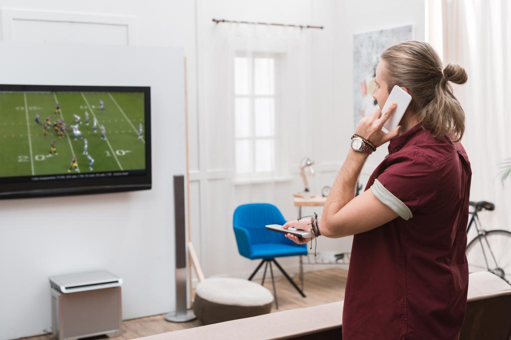 homem falando no smartphone enquanto assiste jogo de futebol em casa
  - Foto, Imagem
