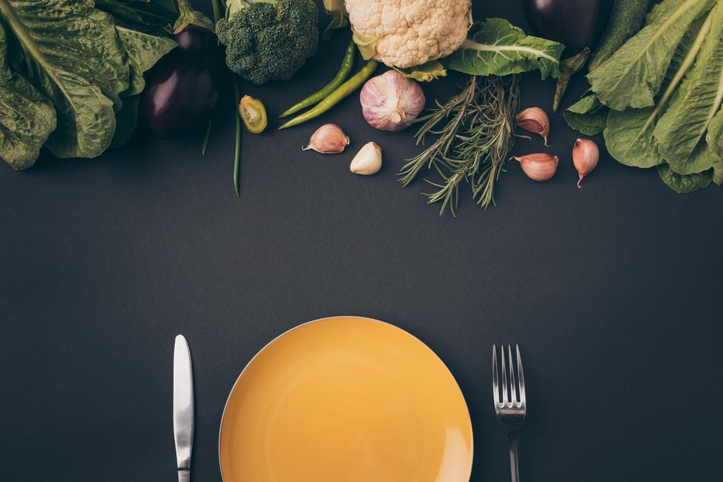 felülnézet, kést, villát és tányér zöldséges szürke felületen - Fotó, kép