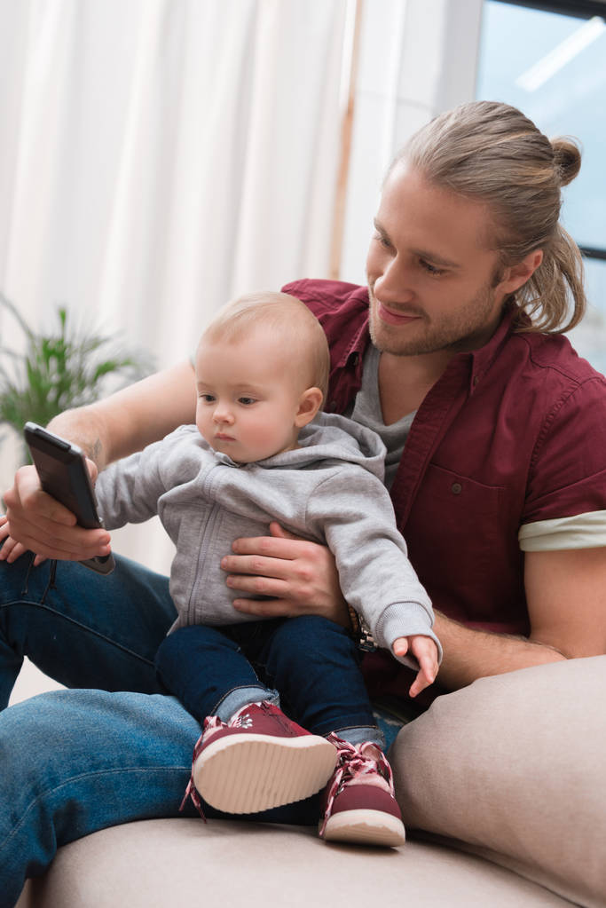 ευτυχής πατέρας κάθεται με το μικρό του γιο και χρησιμοποιώντας το smartphone - Φωτογραφία, εικόνα