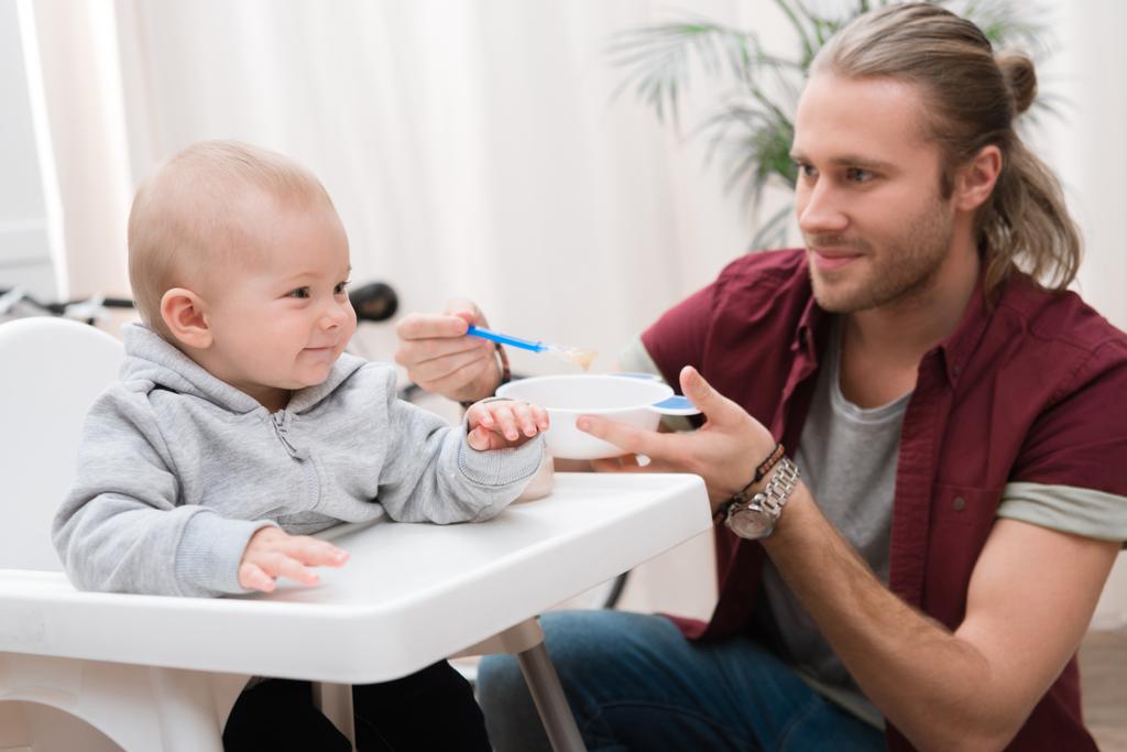 pai alimentando seu filho alegre com comida de bebê em casa
 - Foto, Imagem
