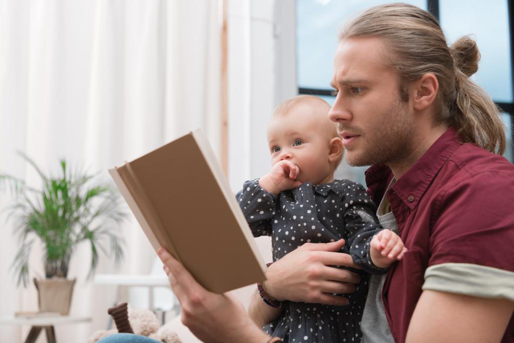 padre leyendo libro a la pequeña hija en casa
 - Foto, imagen