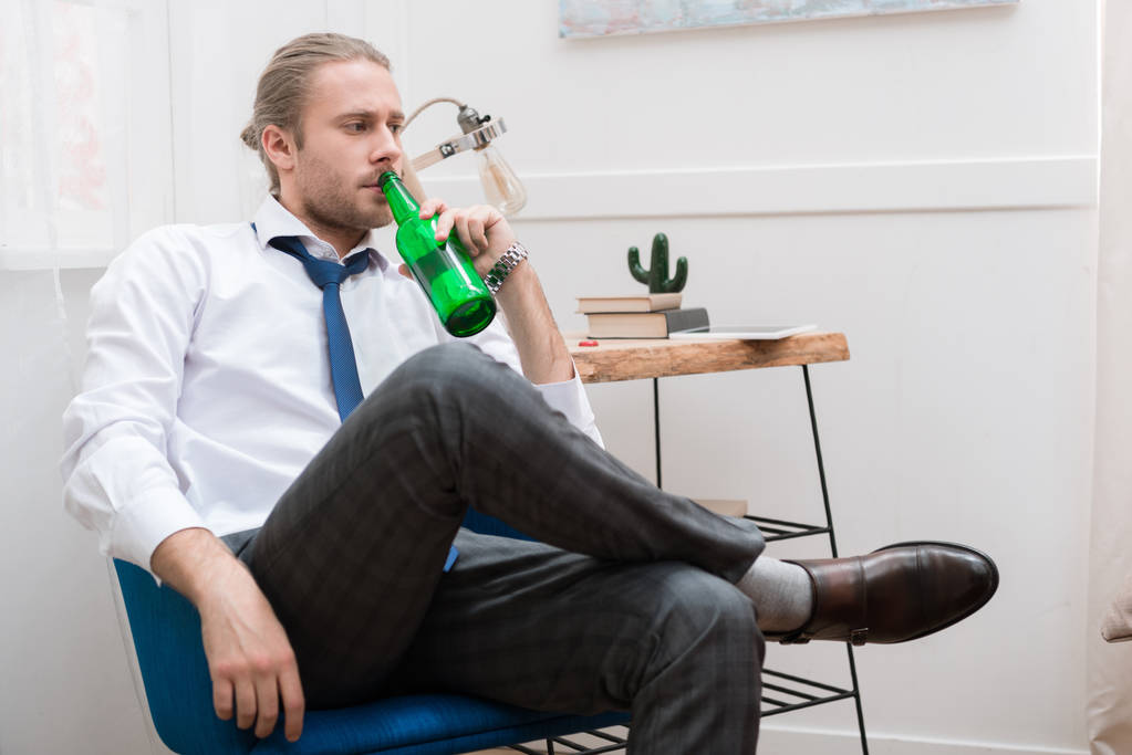 Knappe man, zittend in een stoel en het drinken van bier - Foto, afbeelding