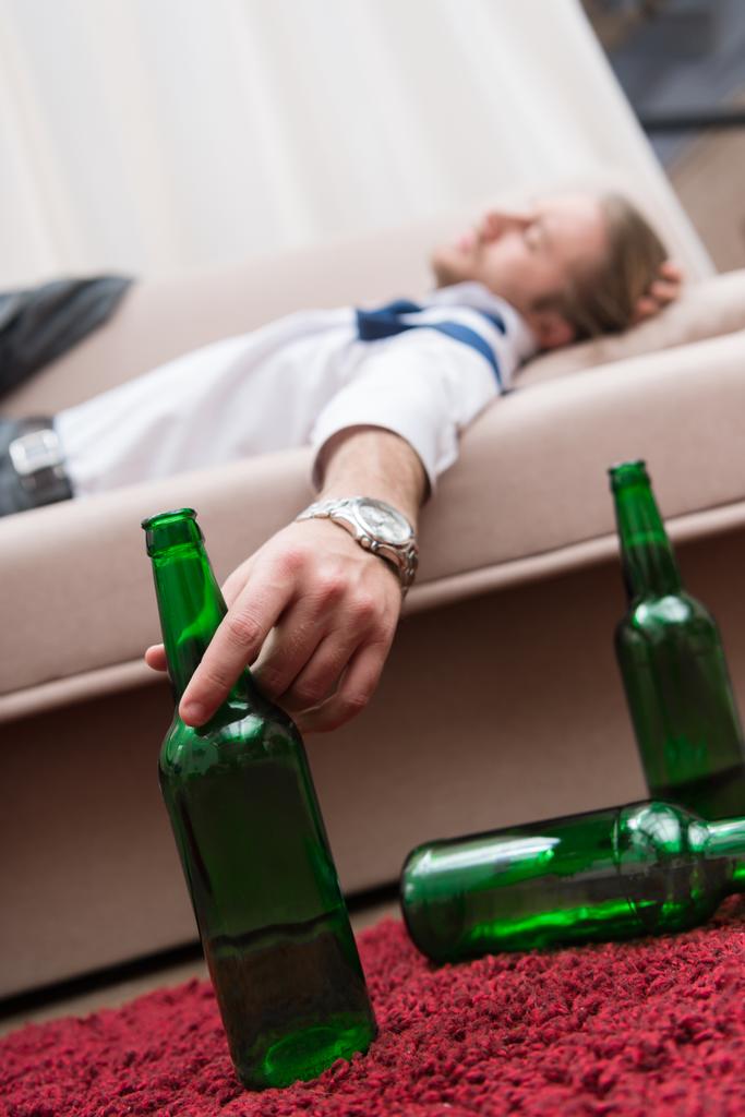 Hombre borracho durmiendo en un sofá y sosteniendo una botella de cerveza
 - Foto, imagen
