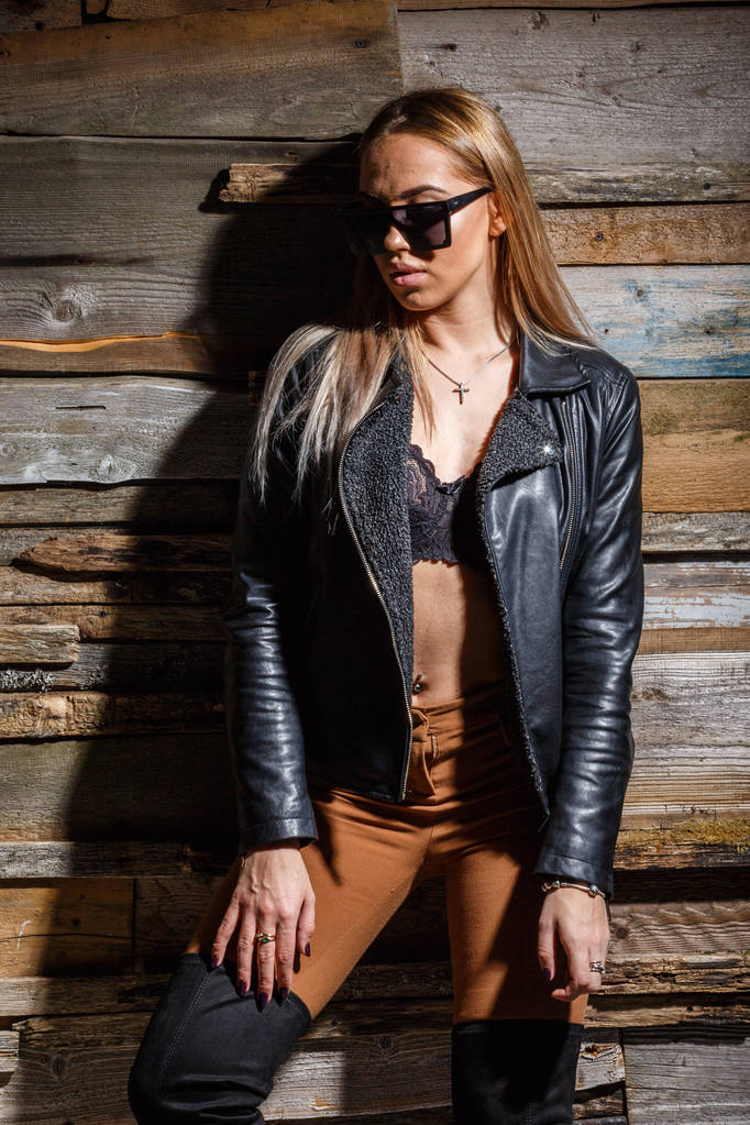 Студийный снимок молодой блондинки. Красотка в стильном бюстгальтере, пиджаке и солнцезащитных очках на фоне гранжевой деревянной стены
  - Фото, изображение
