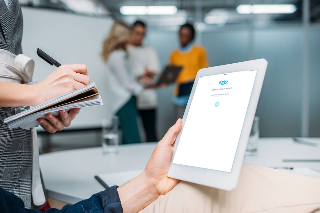 empresário segurando tablet com skype na tela no escritório moderno, enquanto colega fazendo anotações
 - Foto, Imagem