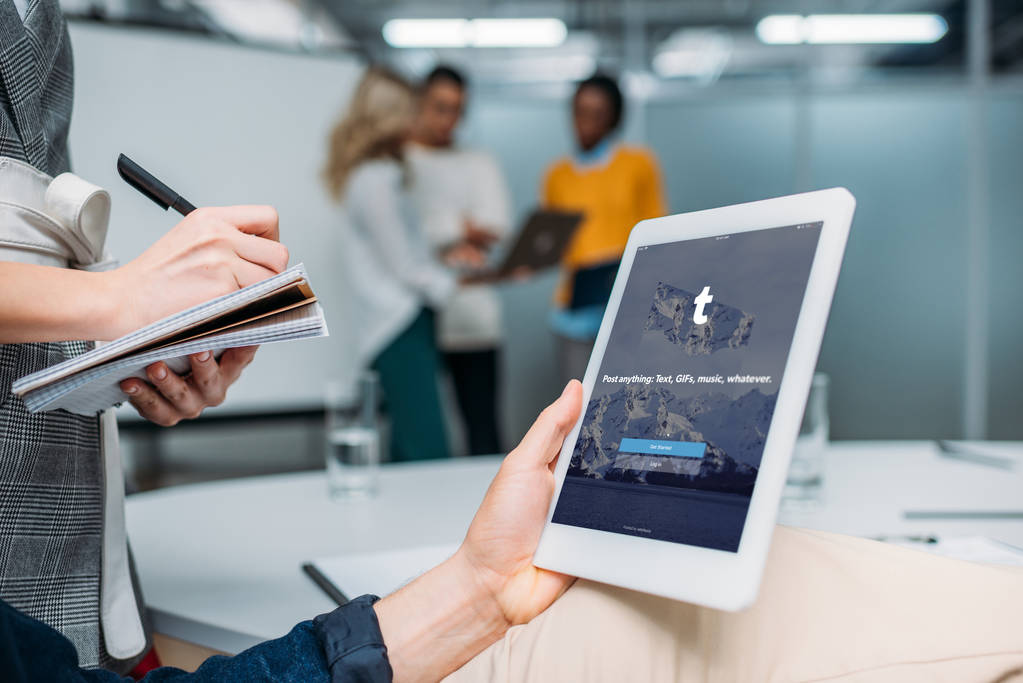бизнесмен держит планшет с tumblr на экране в современном офисе, в то время как коллега делает заметки
 - Фото, изображение