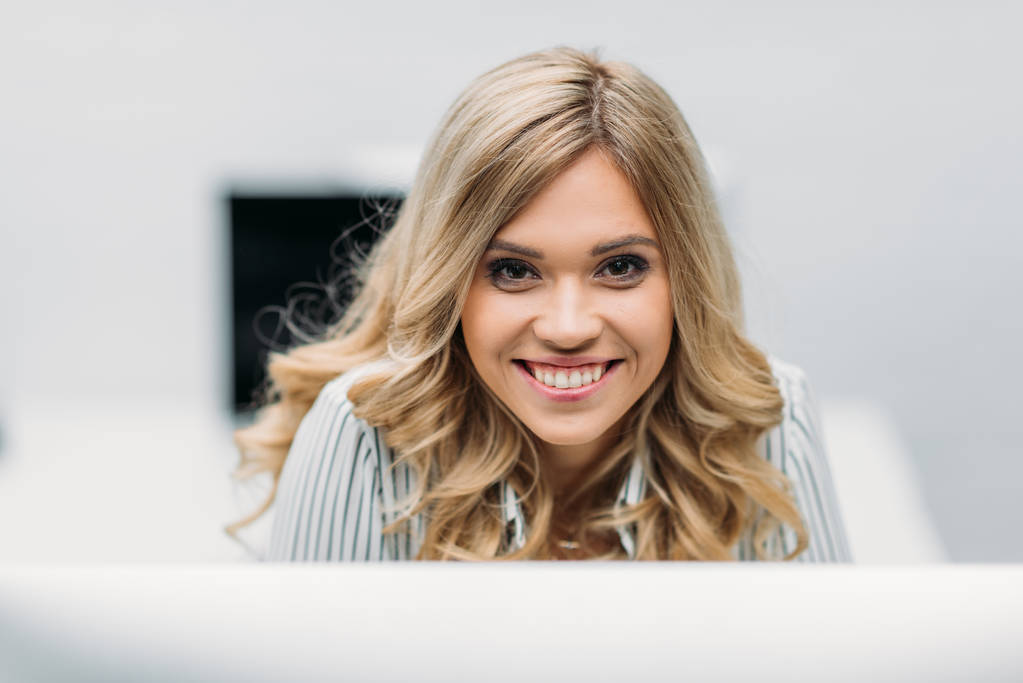 χαμογελώντας νεαρή γυναίκα με ξανθά σγουρά μαλλιά στο γραφείο - Φωτογραφία, εικόνα
