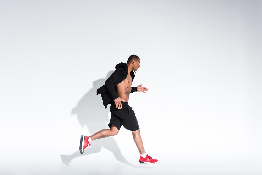 side view of young african american man in sportswear running on grey - Photo, Image