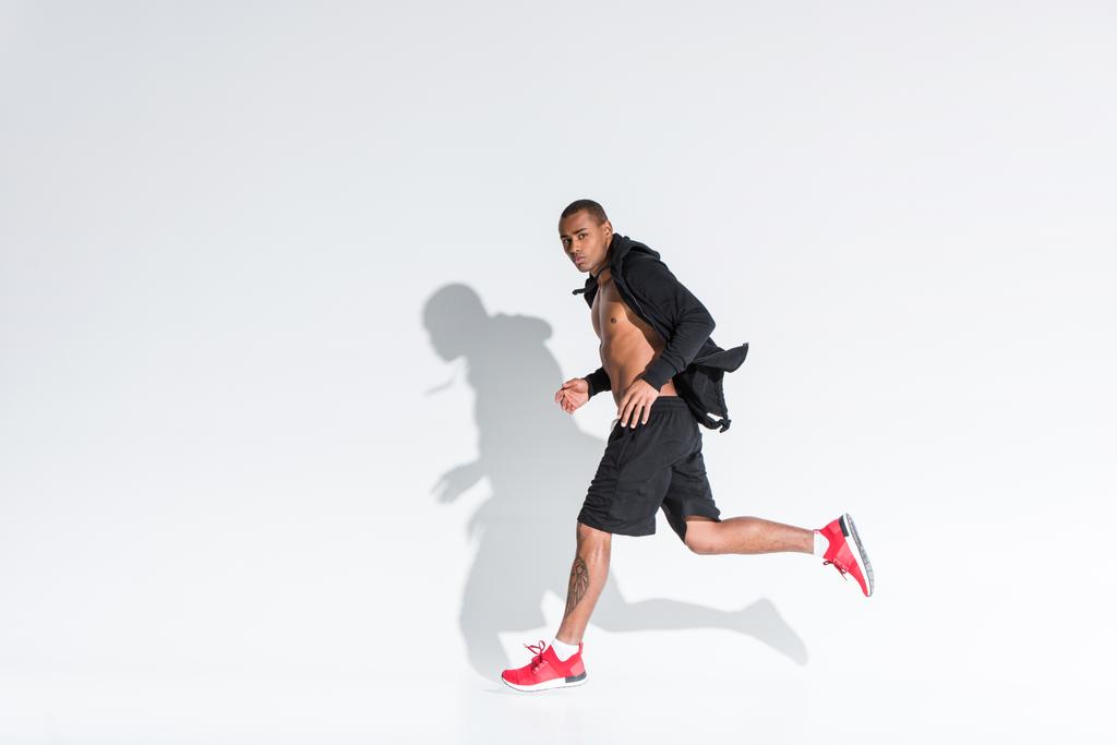 junger afrikanisch-amerikanischer Sportler läuft und schaut in die Kamera auf grau - Foto, Bild
