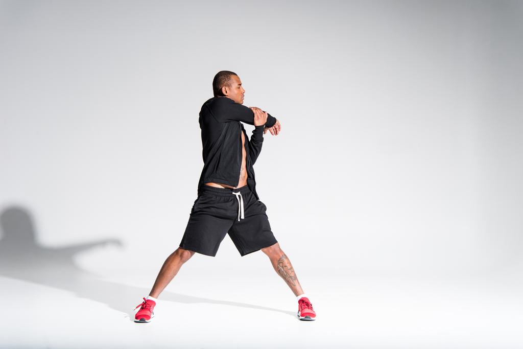 vista completa de joven atlético afroamericano deportista estiramiento en gris
 - Foto, imagen