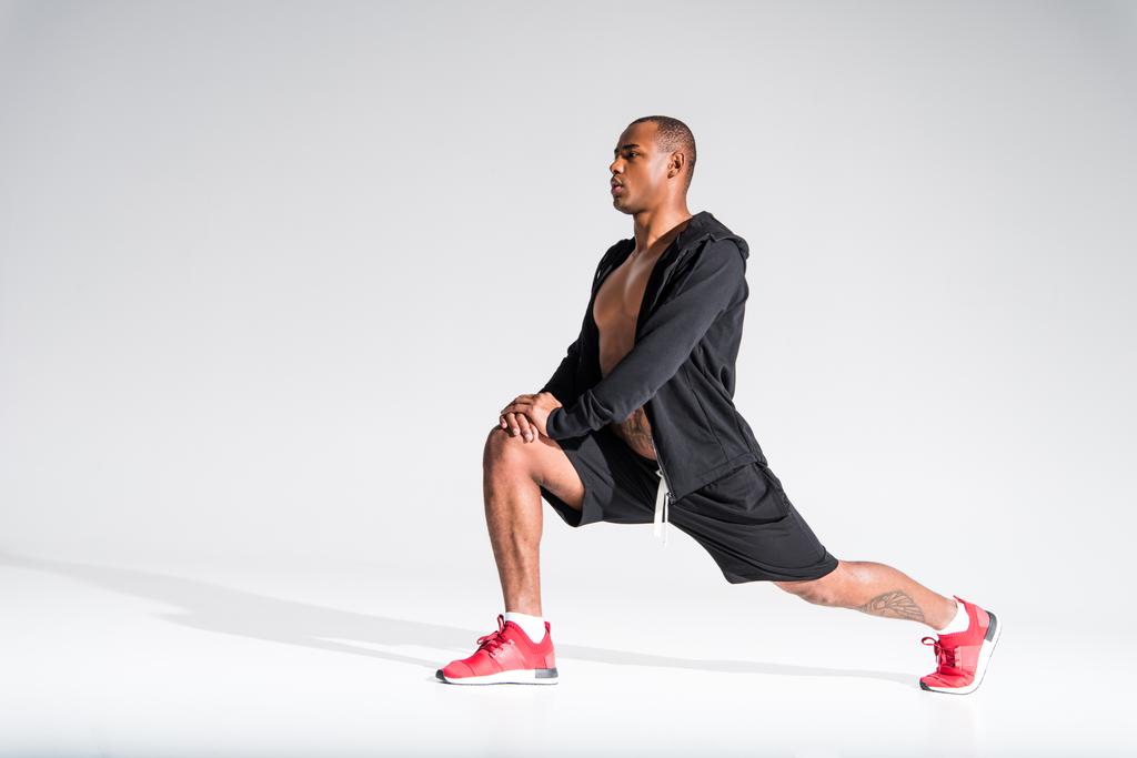 atlético jovem afro-americano desportista esticando e olhando para longe em cinza
 - Foto, Imagem