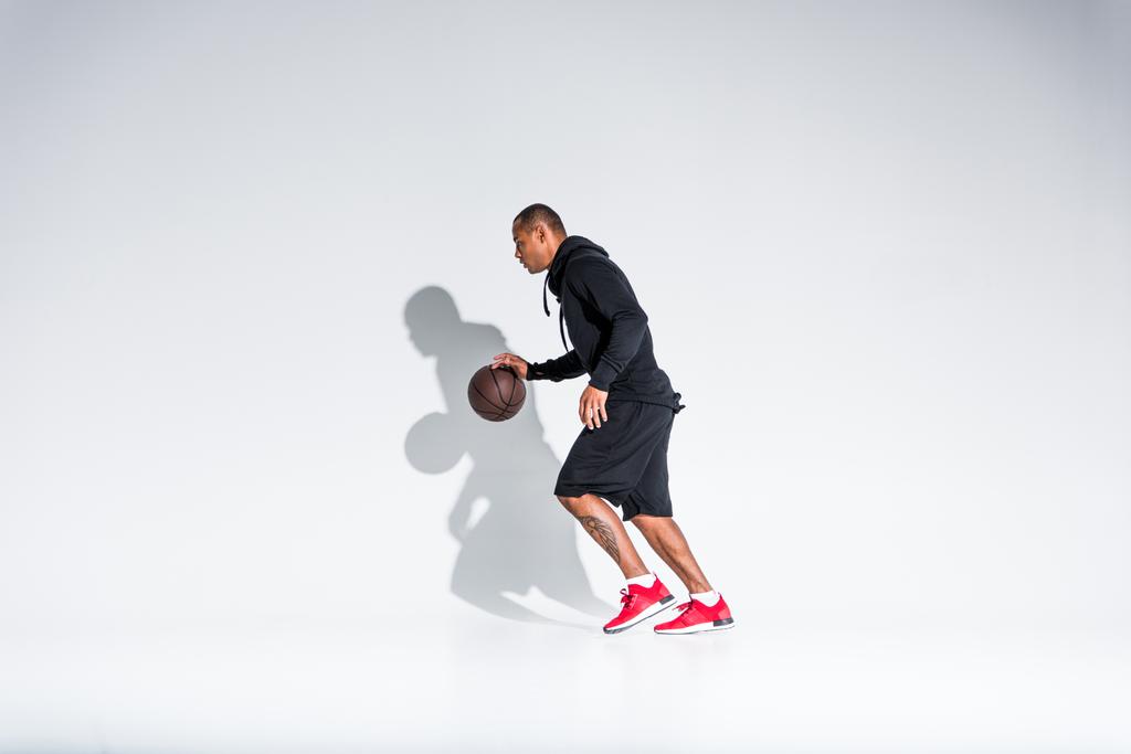 visão de comprimento total do jovem esportista afro-americano jogando com bola de basquete em cinza
  - Foto, Imagem
