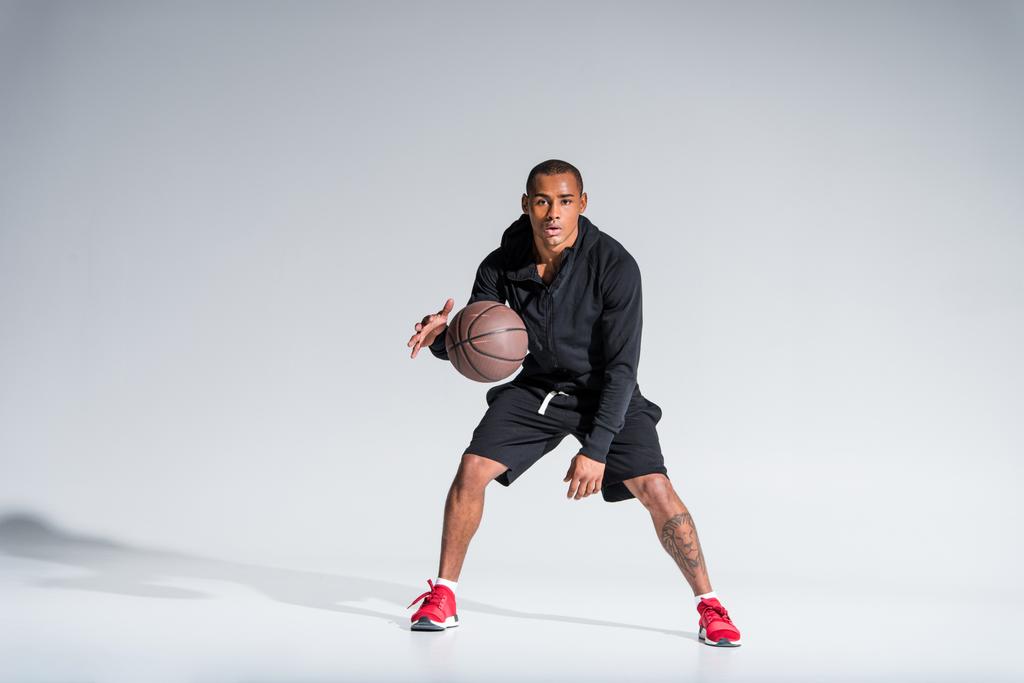 deportivo afroamericano hombre jugando con pelota de baloncesto y mirando a la cámara en gris
 - Foto, Imagen