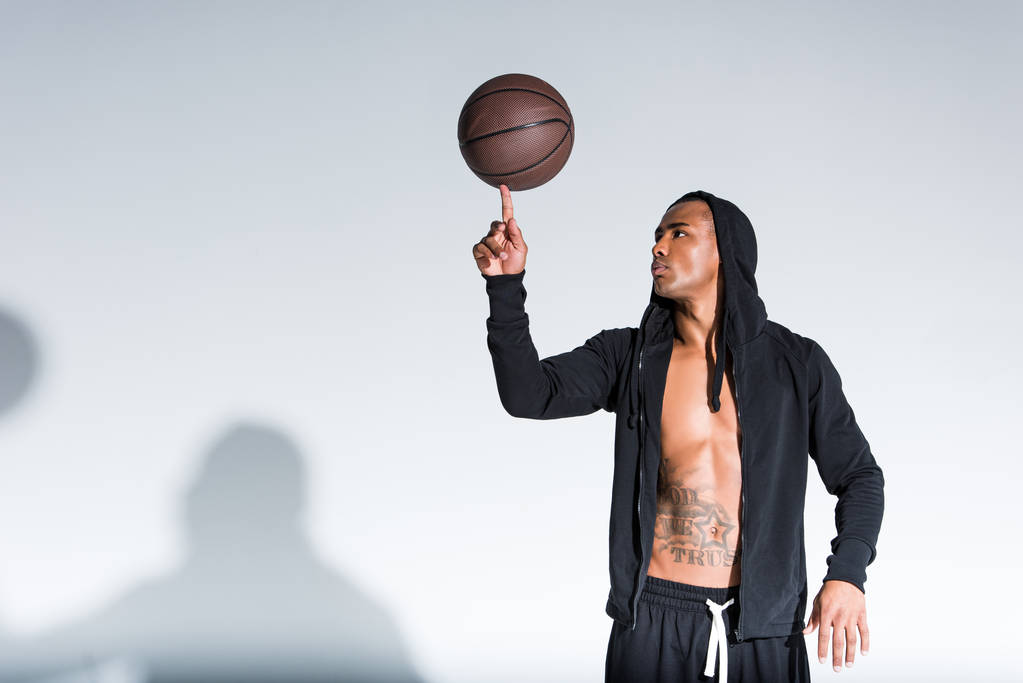 Afrikanisch-amerikanischer Mann hält Basketballball am Finger auf grau - Foto, Bild