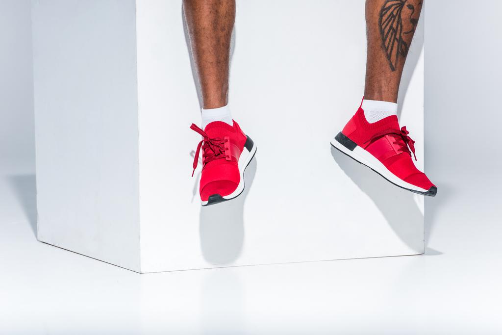 низкая часть африканского американца в красных кроссовках сидит на сером
 - Фото, изображение