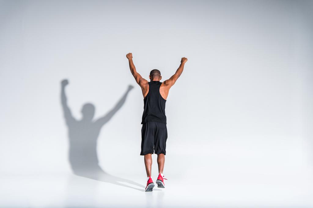 グレーの上げられた手で triumphing 運動のアフリカ系アメリカ人スポーツマンの背面図  - 写真・画像