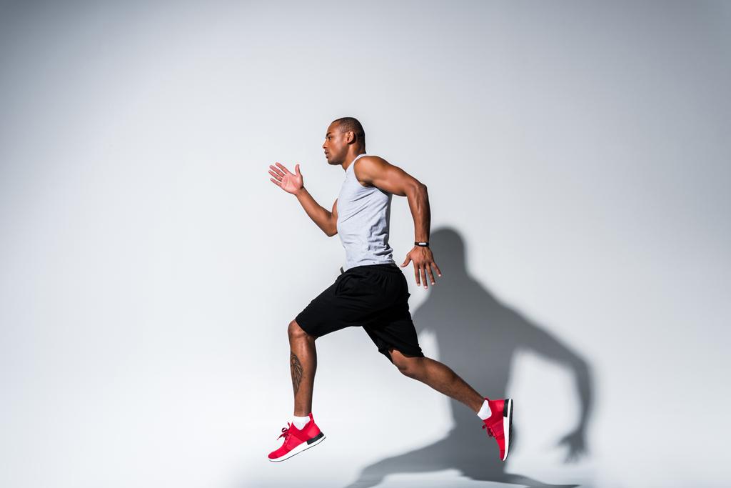 vista laterale del giovane sportivo afroamericano che corre sul grigio
 - Foto, immagini