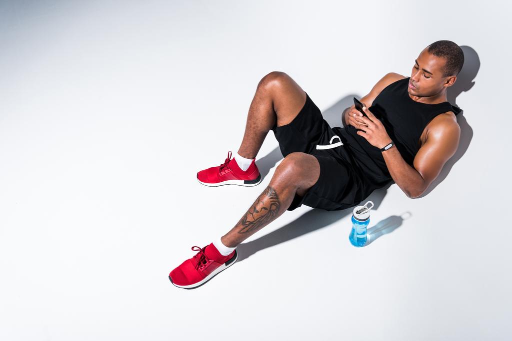 visão de alto ângulo de belo esportista afro-americano usando smartphone em cinza
 - Foto, Imagem