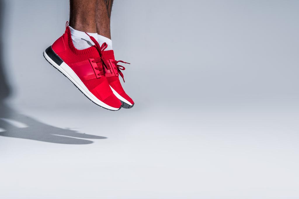 обрізаний знімок молодого афроамериканського спортсмена в кросівках, що стрибають на сірому
 - Фото, зображення