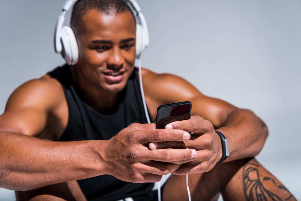 スマート フォンを使用してヘッドフォンでハンサムな笑顔若いアフリカ系アメリカ人のスポーツマン - 写真・画像
