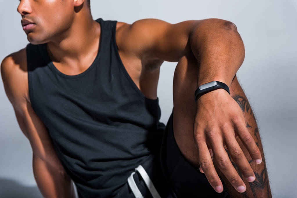 Schnappschuss eines jungen afrikanisch-amerikanischen Sportlers mit Fitness-Tracker auf grau - Foto, Bild