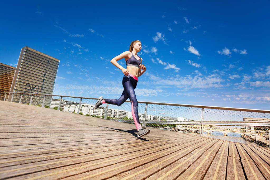 Πλευρά άποψη πορτρέτο του αθλήτρια που τρέχει στην πόλη κατά της μπλε του ουρανού - Φωτογραφία, εικόνα
