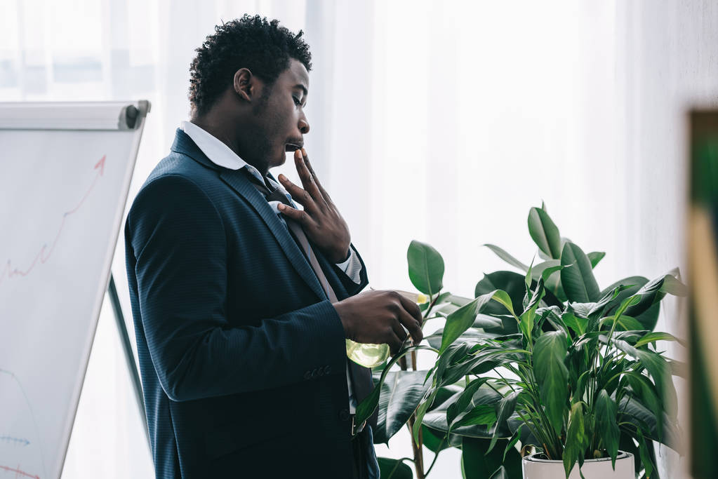 眠いのアフリカ系アメリカ人ビジネスマンがオフィスで植物に水をまく - 写真・画像