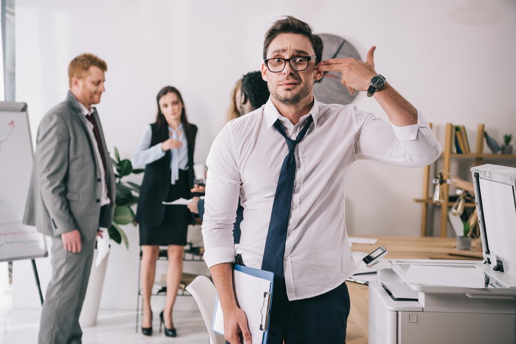 exhausted young manager making handgun gesture at office and looking at camera - Photo, Image