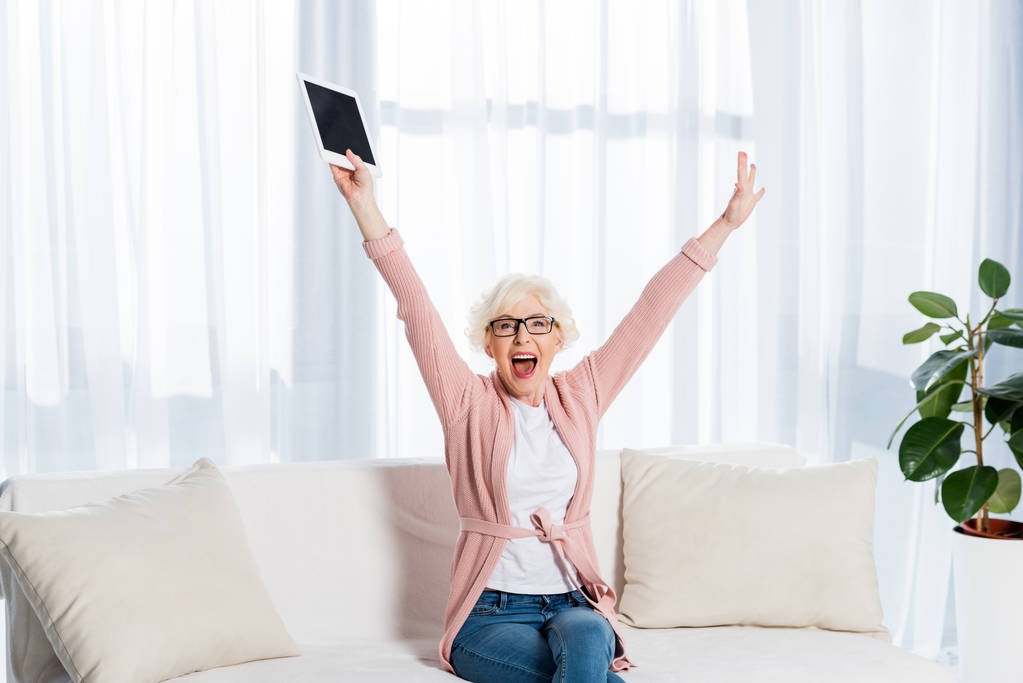 portrét vzrušený starší žena v brýlích s tabletem v ruce při pohledu na fotoaparát doma - Fotografie, Obrázek